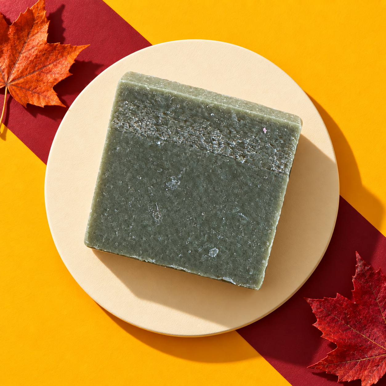 Hometown goat's-milk soap bar, sage green, on a cream plate against marigold and wine