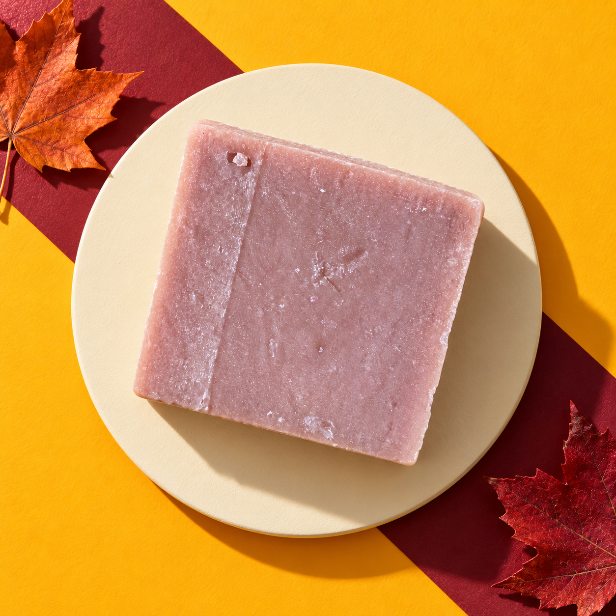 Grandma's Cider goat's-milk soap bar, dusty rose, on a cream plate against marigold and wine